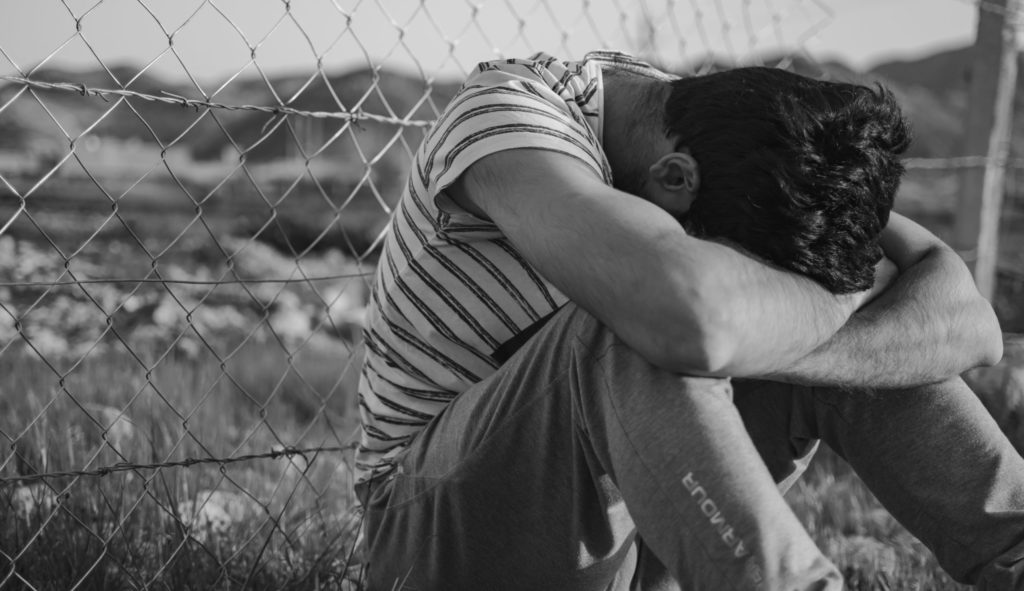 man in black and white stripe t-shirt leaning on chain link fence
