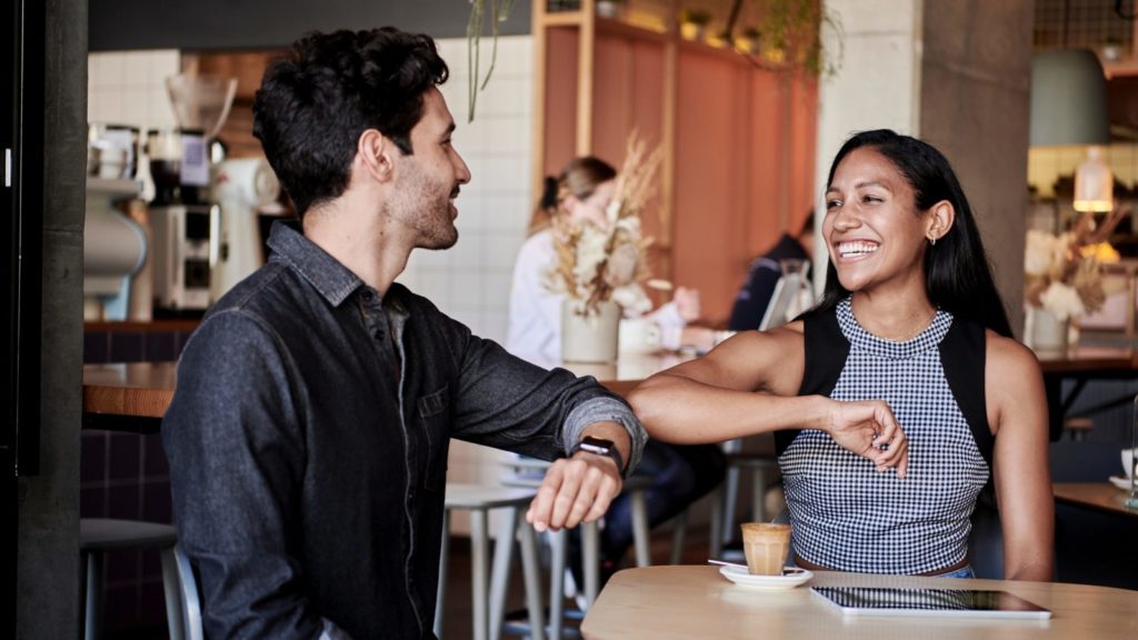 man in black shirt elbow bumping with woman in a restaurant