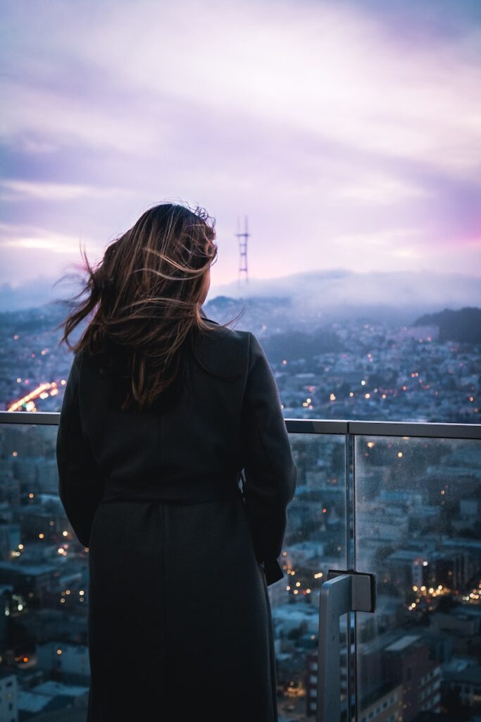 woman in black coat standing on top of building looking at the city during daytime
