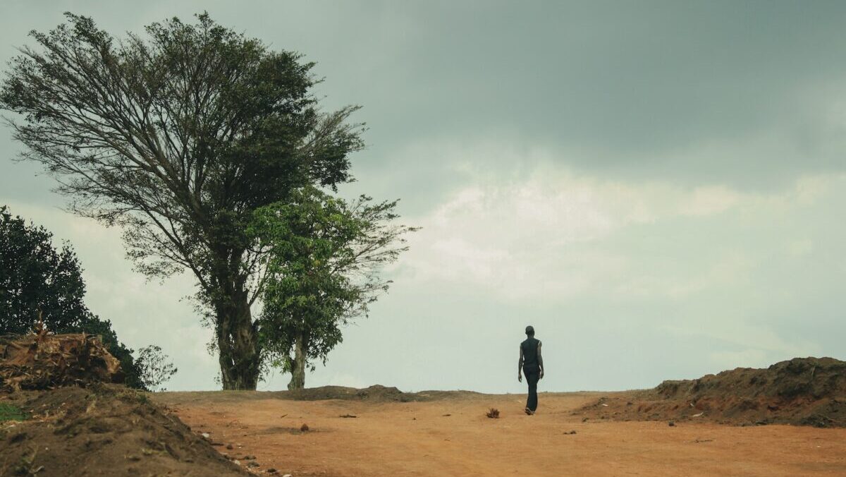 man in black jacket walking on brown sand near green tree during daytime