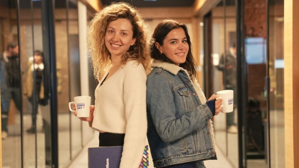 two women standing in a hallway holding coffee mugs