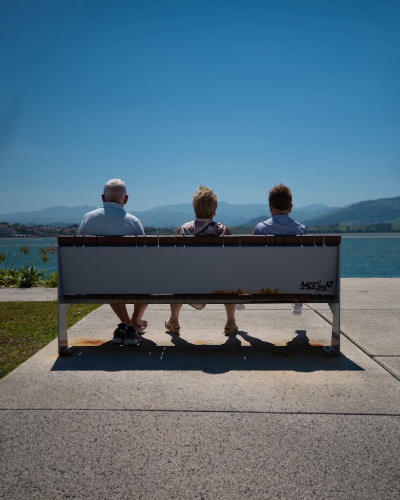 three people sitting on a bench looking at the water