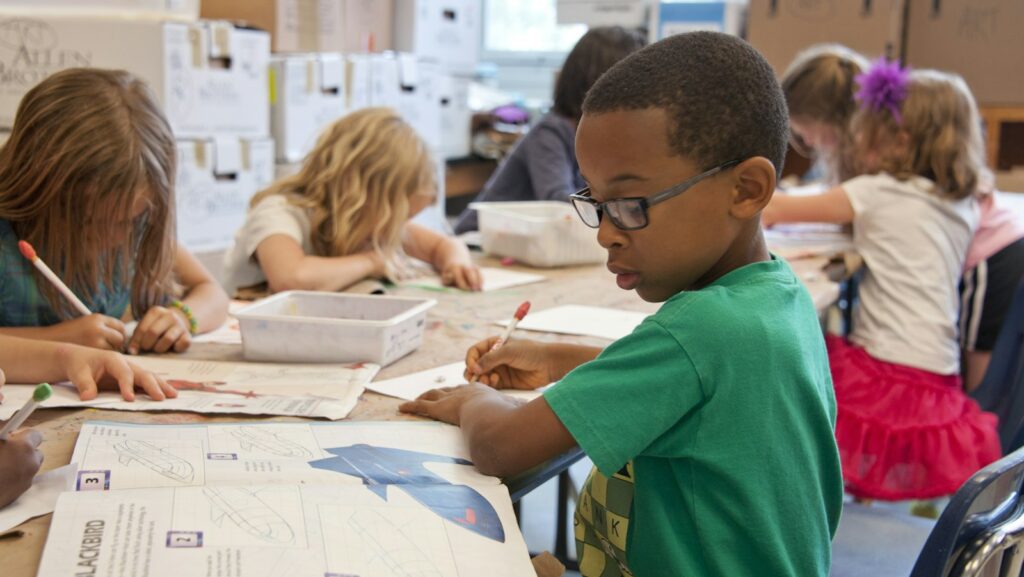 boy in green sweater writing on white paper
