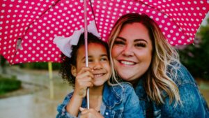 Adult female and young girl smiling under pink polka dot umbrella