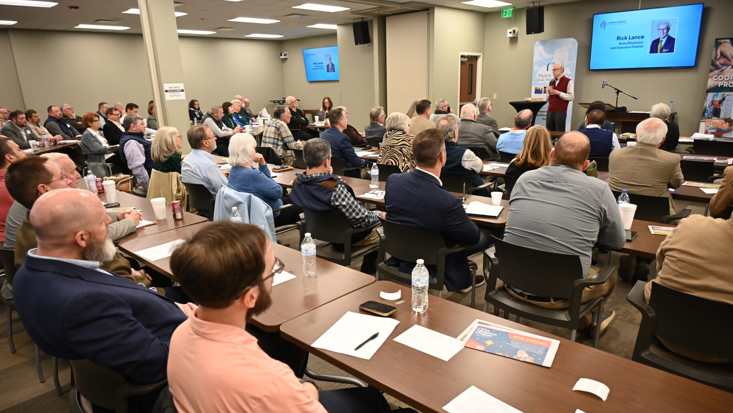 Room filled with people sitting in rows facing speaker at the front