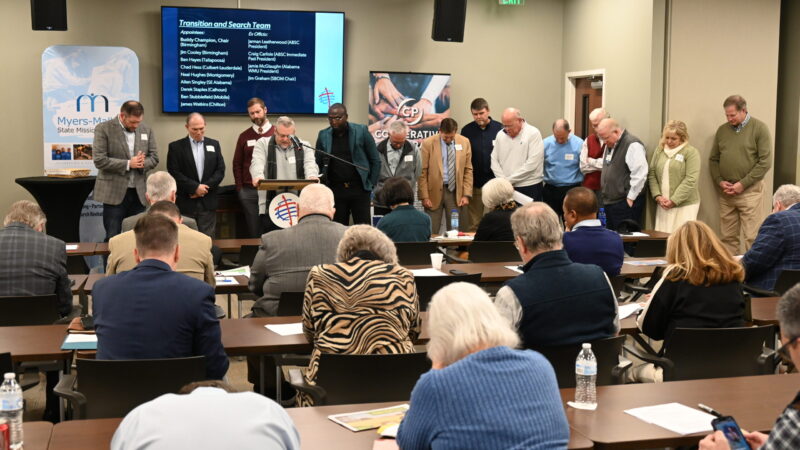 Meeting room with some people sitting and some standing at the front of the room.