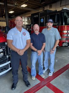 Three men standing in front of fire trucks